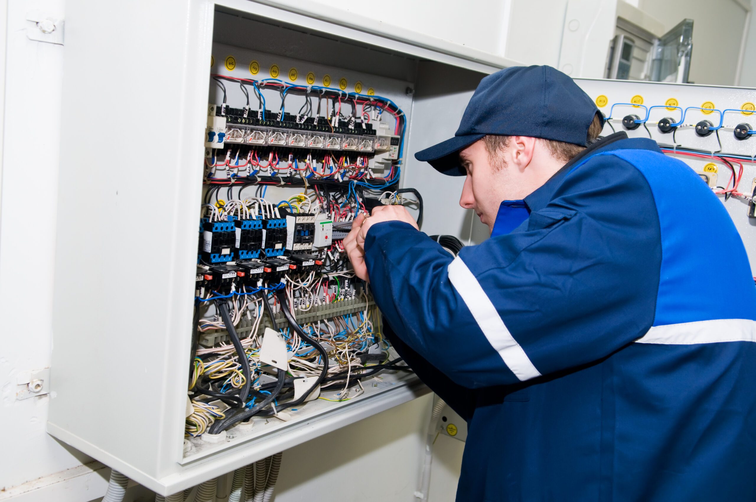 A Man in a Blue Uniform Working on a Panel.
